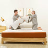 couple playing pillow fight on their mattress